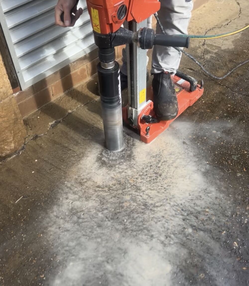Doctor Pesty technician core-drilling through a concrete slab to install an in-ground termite monitoring station